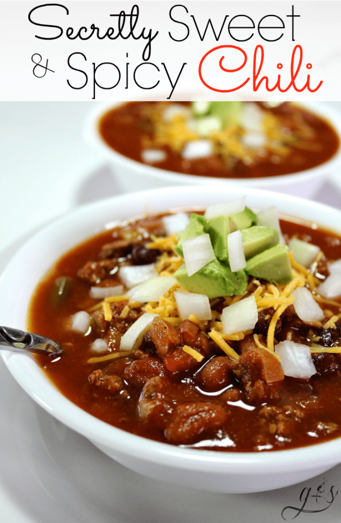 Two bowls of a Sweet and Spicy Chili recipe topped with shredded cheese, diced onion, and avocado.