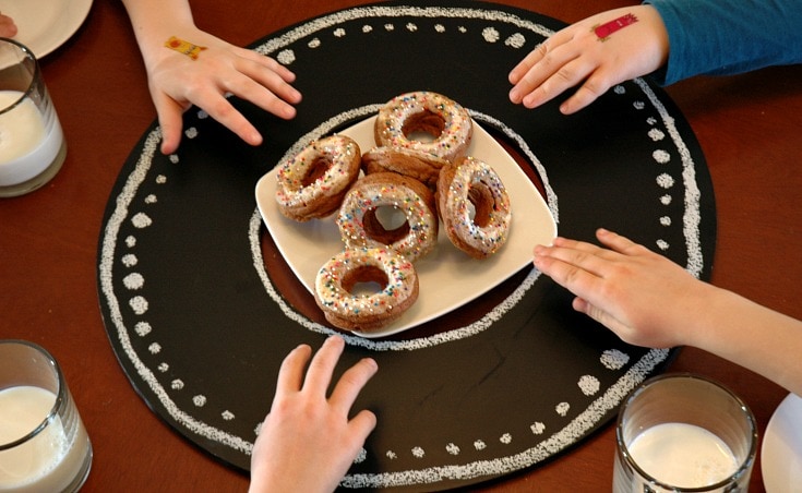 Four little hands of children reaching for donuts made by their moms. 