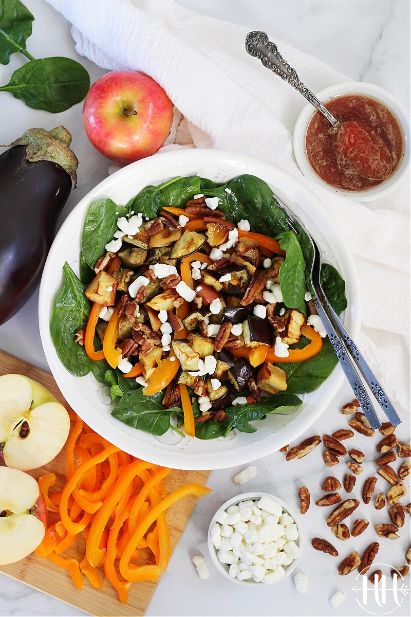 Salad loaded with bell pepper, crumbled goat cheese, and roasted veggies in a white bowl. 