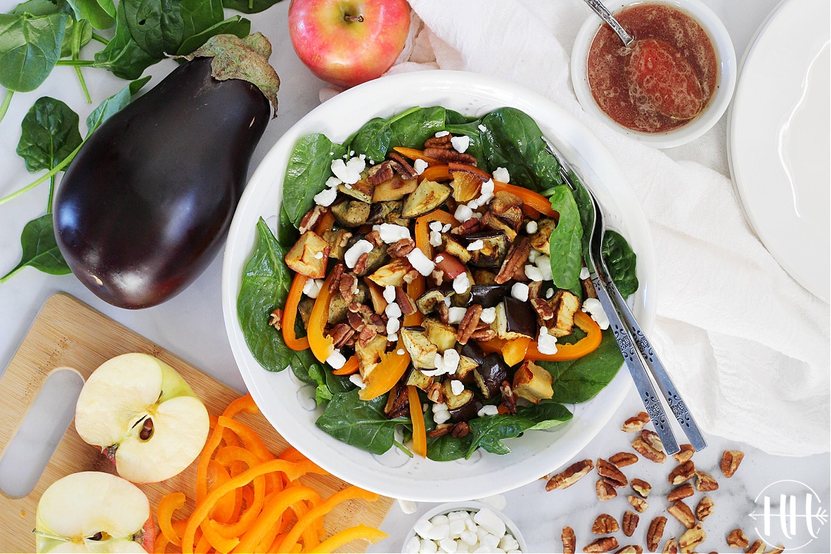 Birds eye view of an Eggplant, Apple, and Spinach Salad with the dressing on the side. 