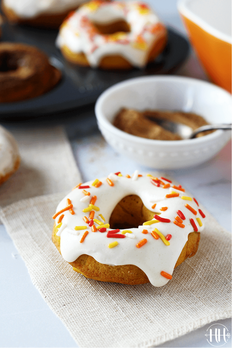 A pretty pumpkin doughnut topped with a cream cheese glaze and autumn sprinkles.