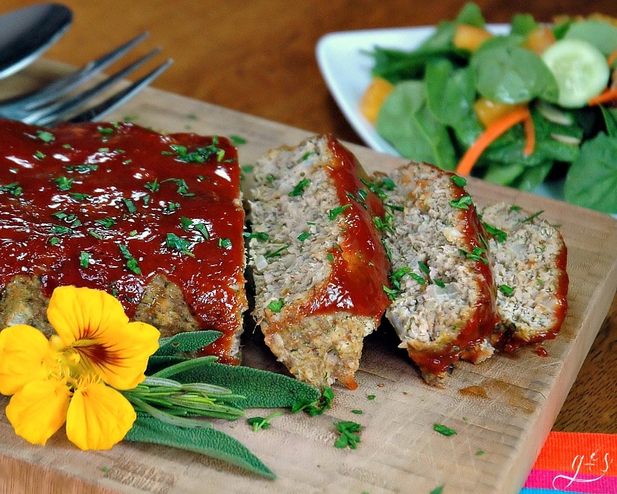 A meatloaf glazed with ketchup and chopped parsley on a cutting board.