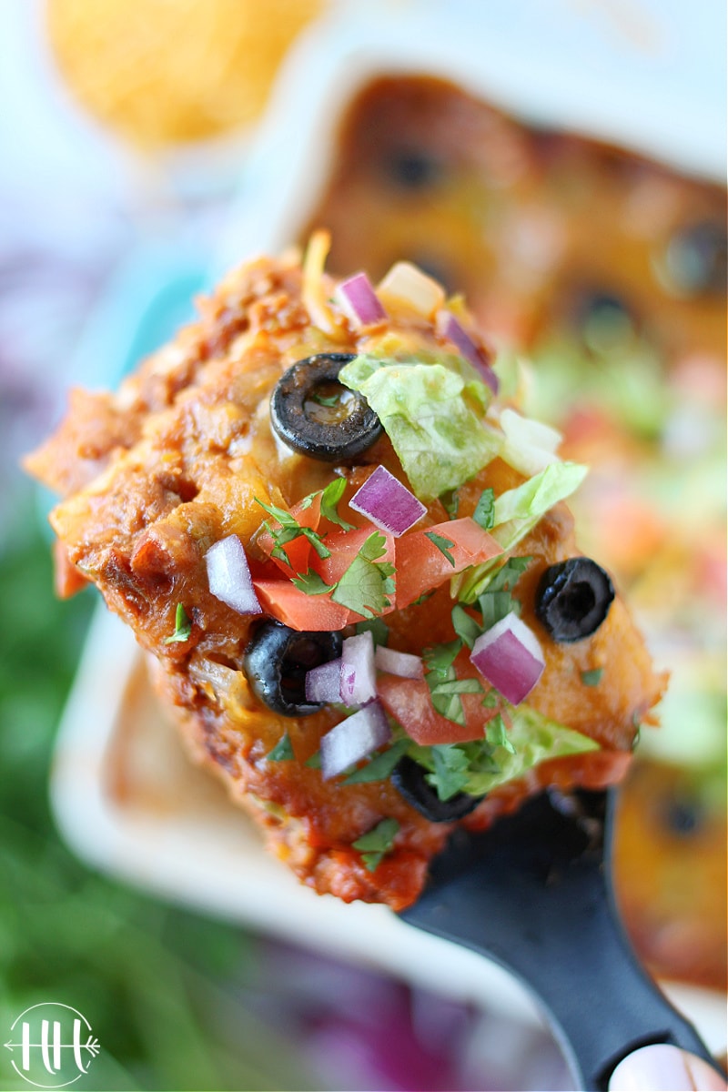 A bird's eye view on a piece of Mexican Lasagna with lettuce, red onion, and olives.