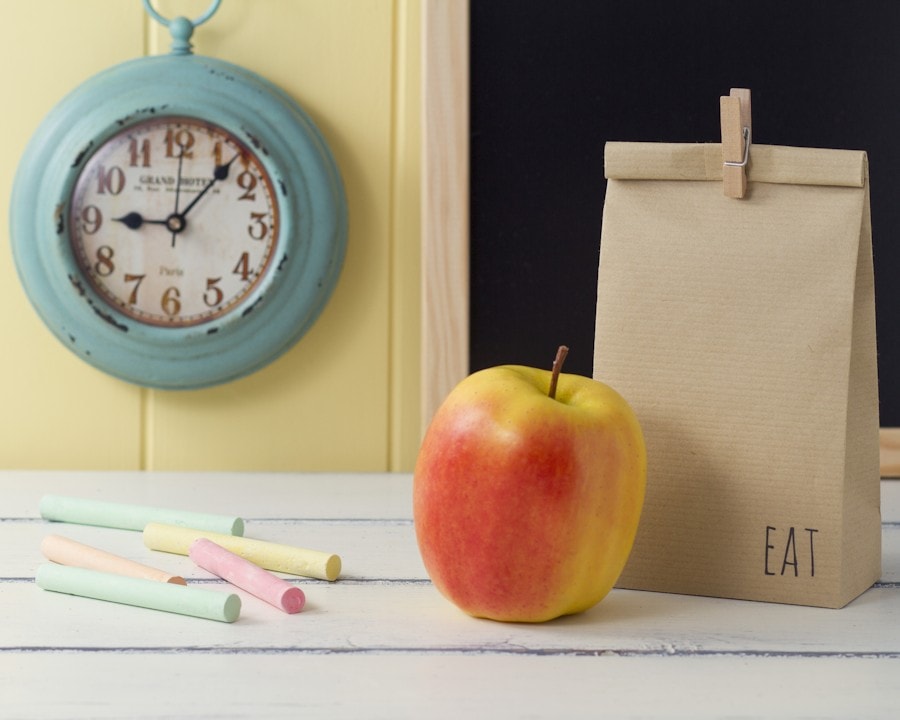 A clock, apple and brown lunch bag with colorful chalk.