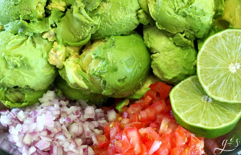 Guacamole, red onion, tomatoes, and lime ready to be mixed.