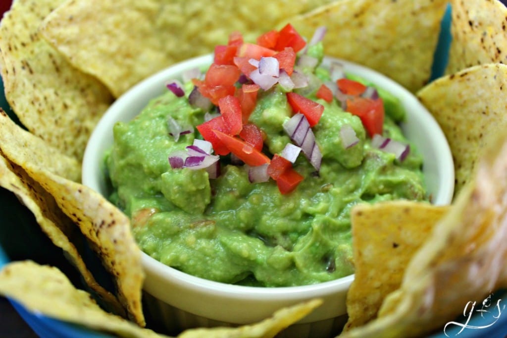 Learn how to make guacamole with a secret ingredient! Here is a bowl of guacamole topped with tomatoes and red onion.