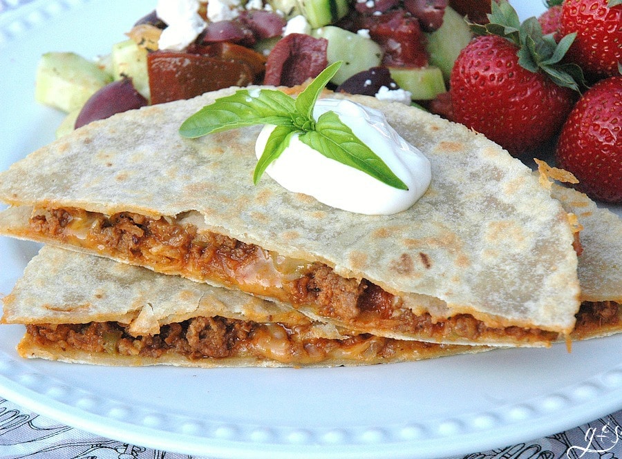 A sloppy joe quesadilla cut in half and stacked topped with sour cream.