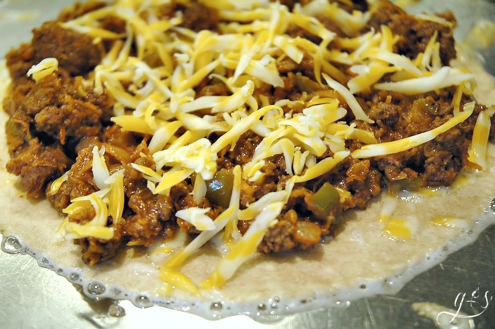 A tortilla topped with homemade sloppy joe mixture and cheese on a hot pan.