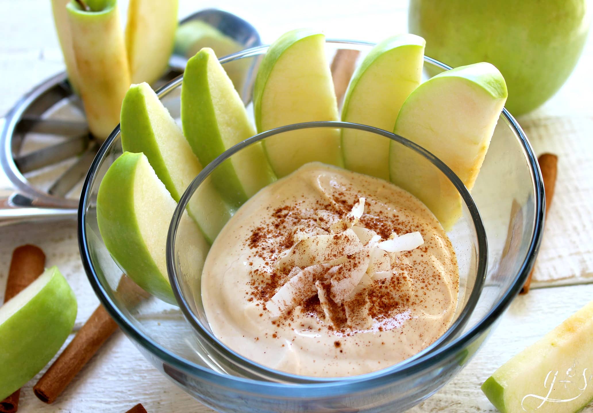 Clear glass bowl of PB2 fruit dip sprinkled with cinnamon with green apples