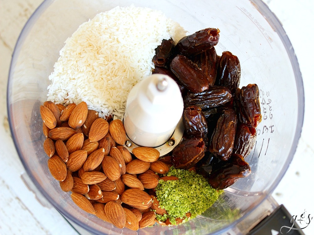 A food processor with whole almonds, pitted dates, unsweetened shredded coconut, and lime zest.