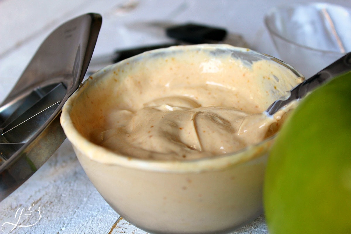 A spoon mixing Greek yogurt and powdered peanut butter in a clear glass bowl.