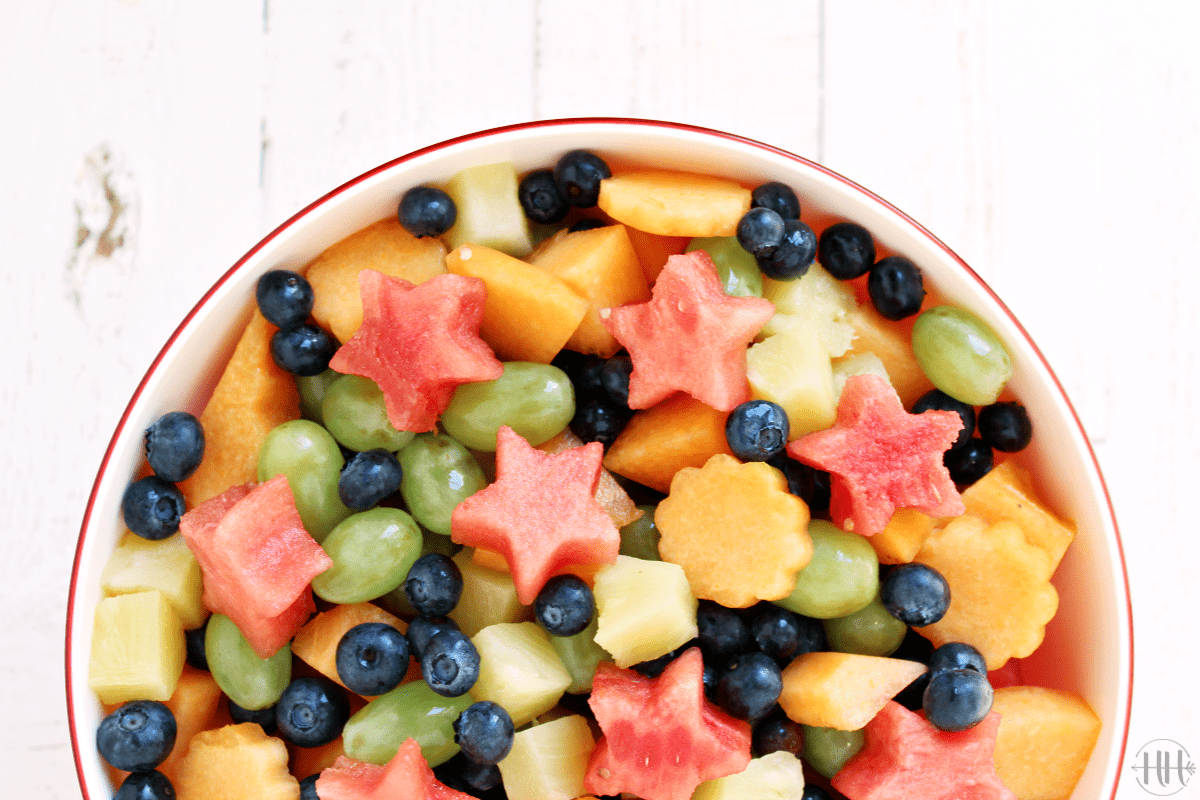 A big bowl of watermelon shaped like stars, cantelope, blueberries, green grapes, and pineapple.