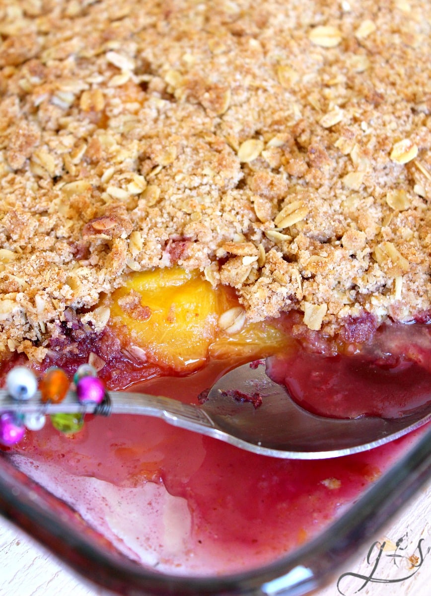 Pan of healthy peach and blueberry crumble with a pretty spoon. 