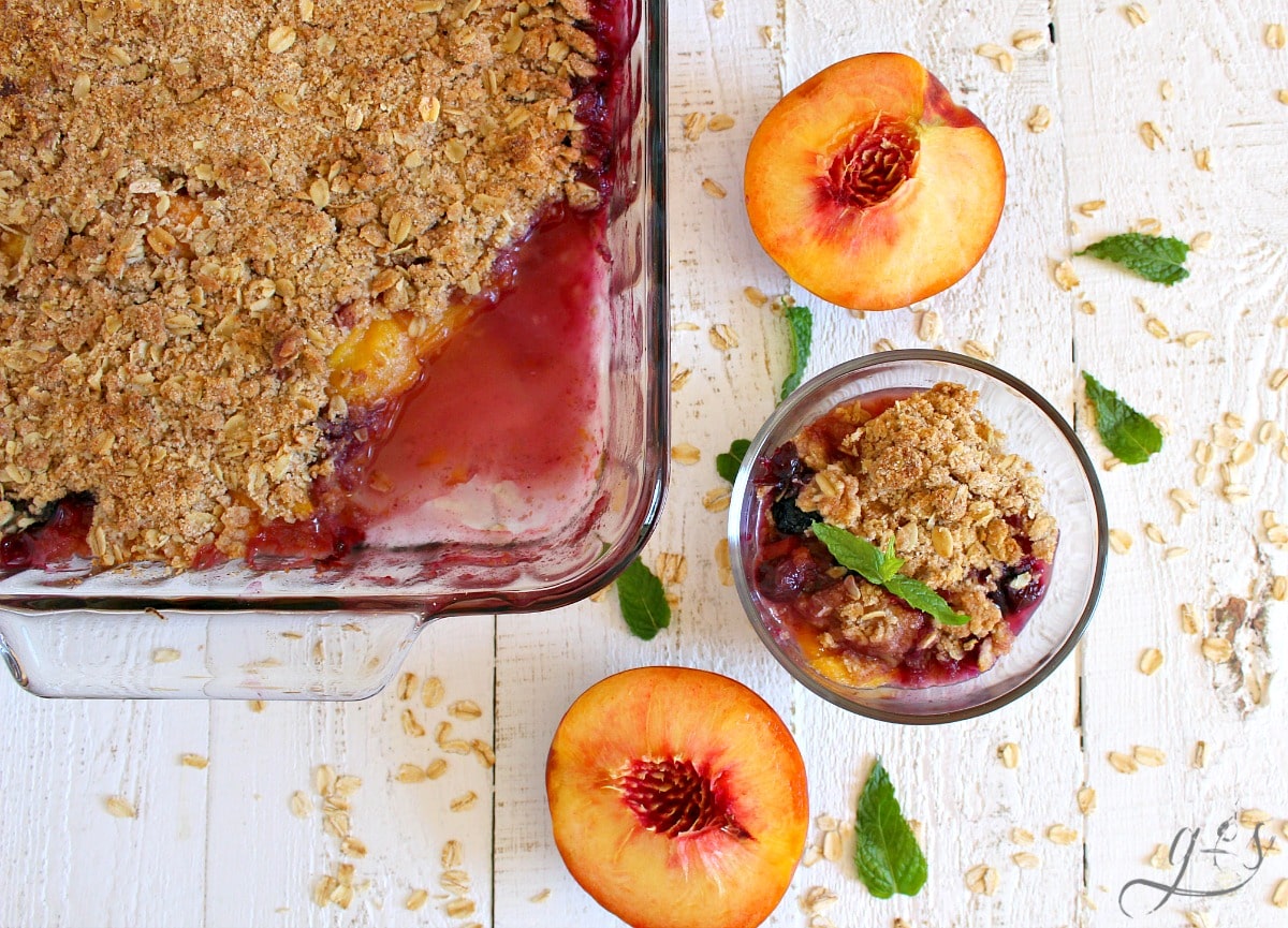 Beautiful pan of peach and blueberry crisp and a prepare bowl with a mint leave on top. 