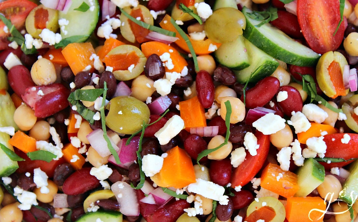 Up close photo of beans, vegetables, basil, and feta cheese in a tangy dressing.