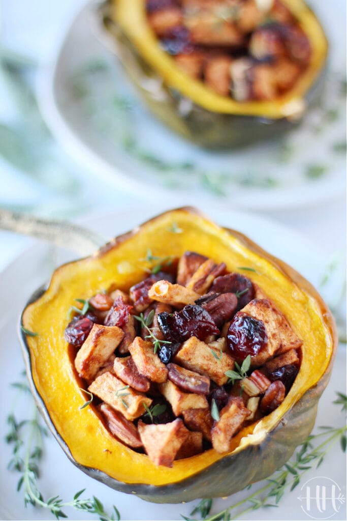 Baked vegetarian stuffed acorn squash on plates with fresh thyme.