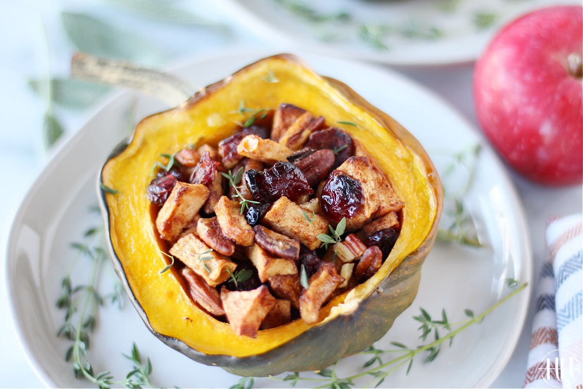 A half of an acorn squash stuffed with apples and pecans on a pretty white plate. 