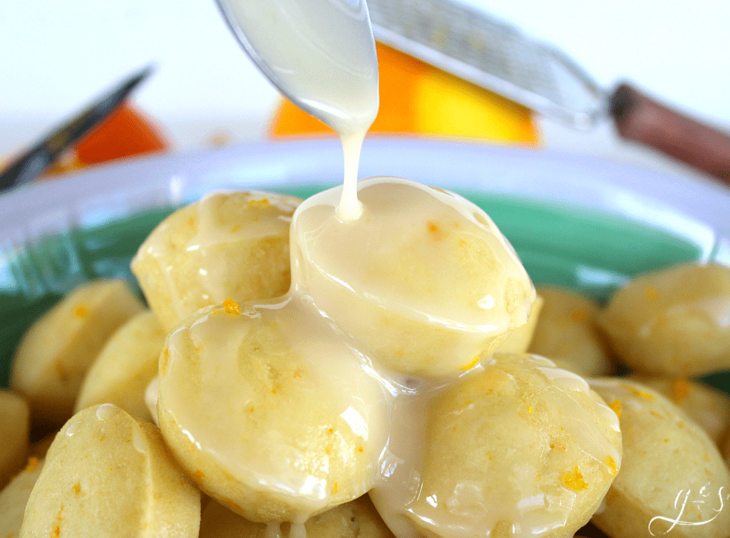 A creamsicle glaze being poured over mini pancake muffins in a bowl.