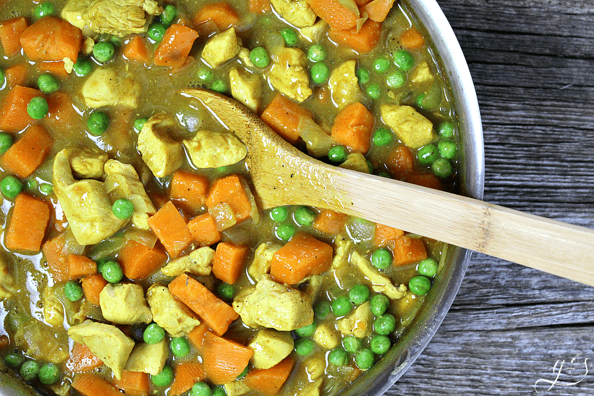 A pan of Clean Eating Chicken & Sweet Potato Curry ready to serve with a wooden spoon. 