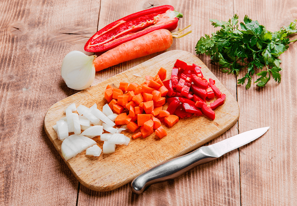 Diced onion, carrots, and bell pepper on a cutting board with fresh parsley.