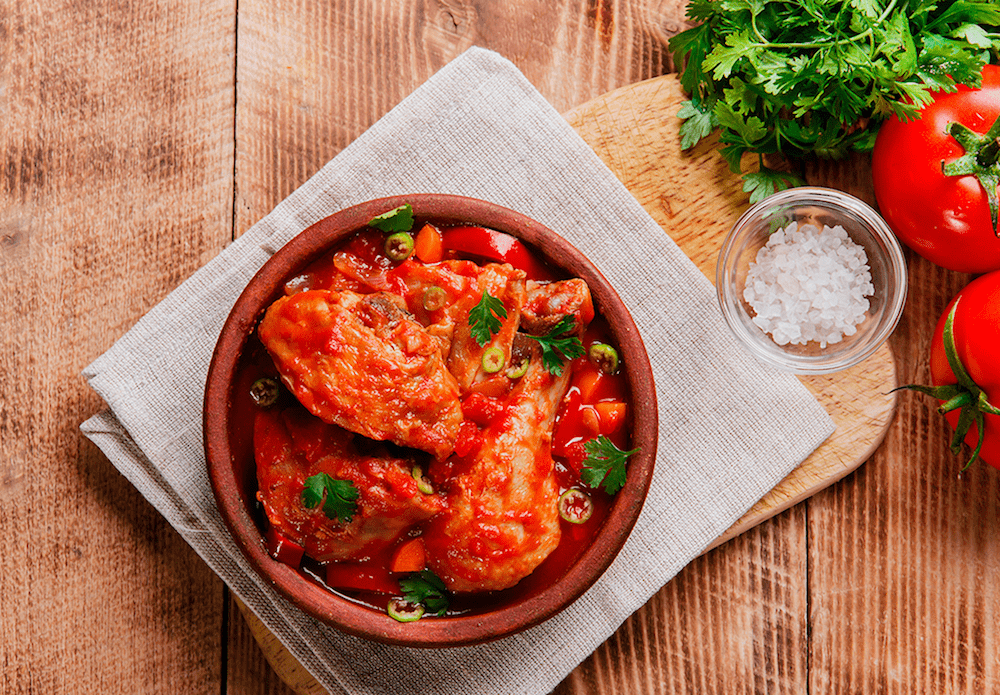 A Chicken & Tomato Chakhokhbili stew in a bowl garnished with green onion and parsley.