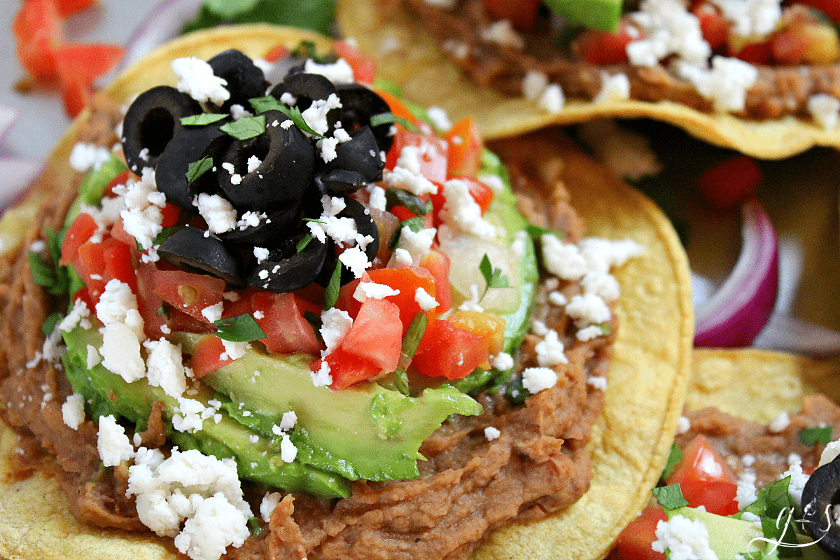 Up close view of a fried tortilla, refried beans, and all the toppings.