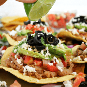 A lime wedge being squeezed over a vegetarian tostada.