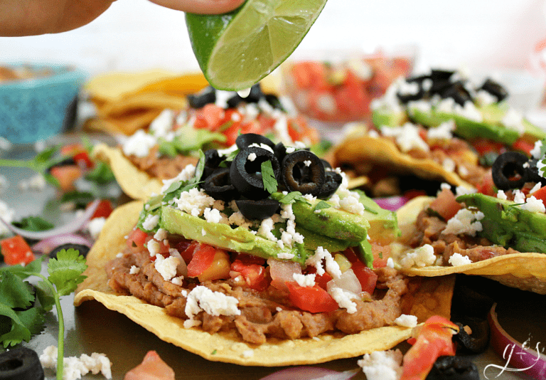A lime wedge being squeezed over a vegetarian tostada.