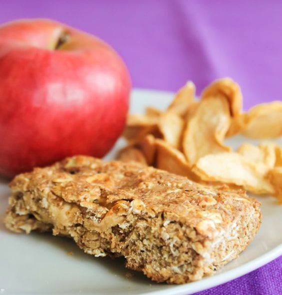 An Apple Cinnamon Breakfast Bar along with a fresh apple and dried apples on a white plate.