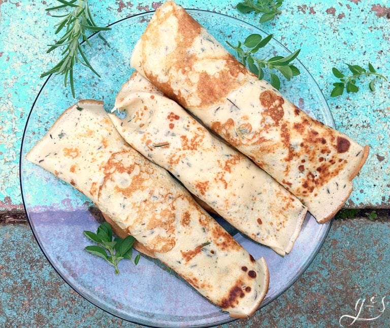 Three crepes stuffed with garden veggies and herbs on a glass plate.