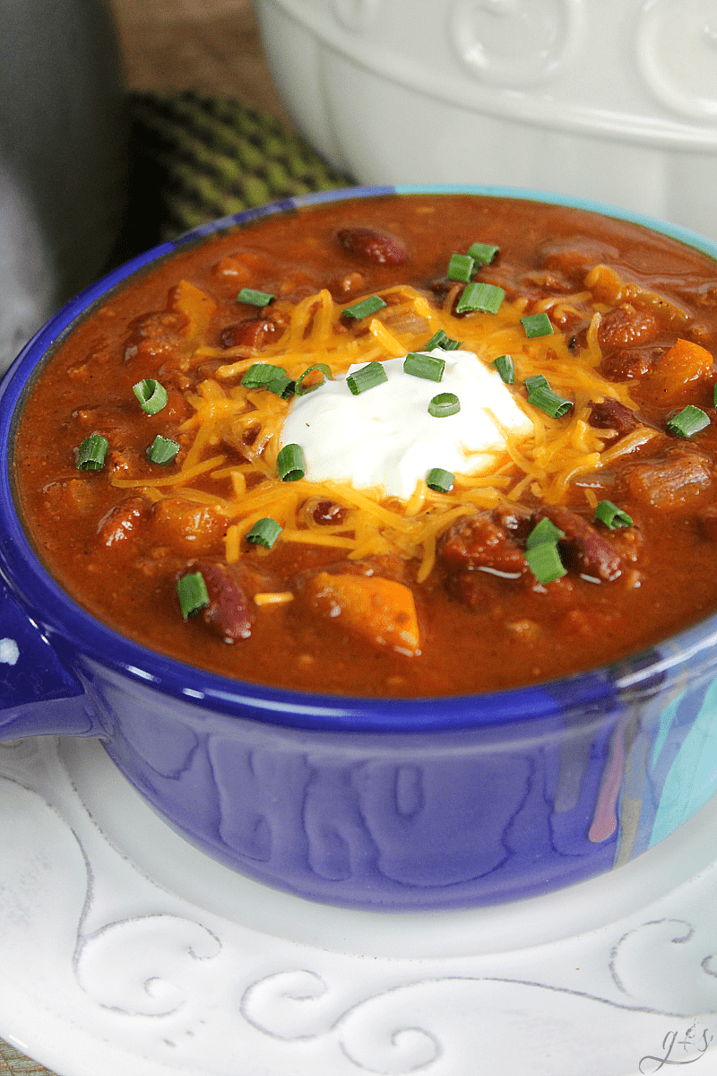 Clean Eating Pumpkin Chili with whole food ingredients and tons of fall flavor in a handmade blue ceramic bowl. Chili is topped with sour cream, shredded cheese, and green onion.