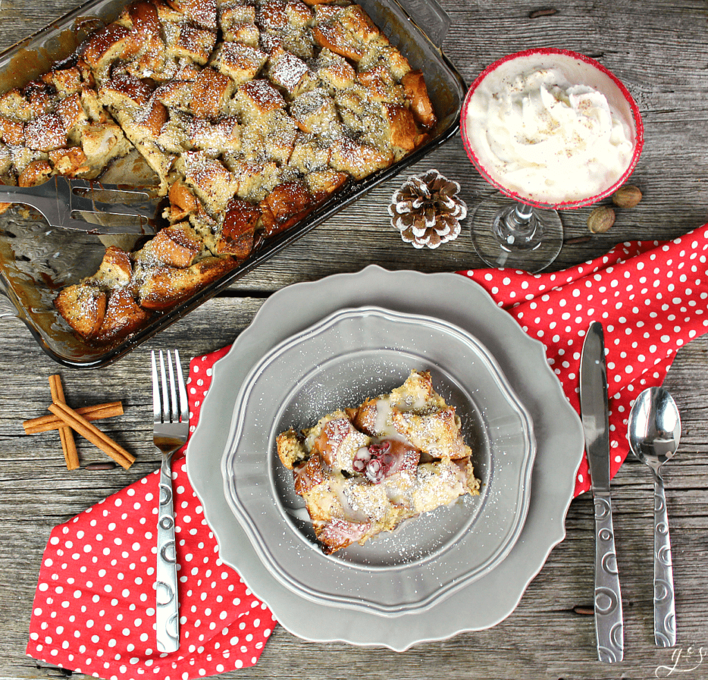 Eggnog french toast casserole in a pan with a piece taken out and put on a plate sprinkled with powder sugar. 