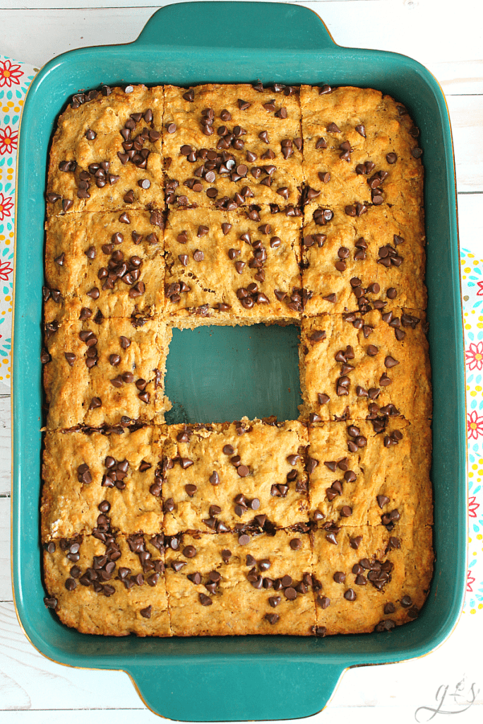 9x13 pan of banana bread blondies topped with mini chocolate chips and one bar missing from the middle.