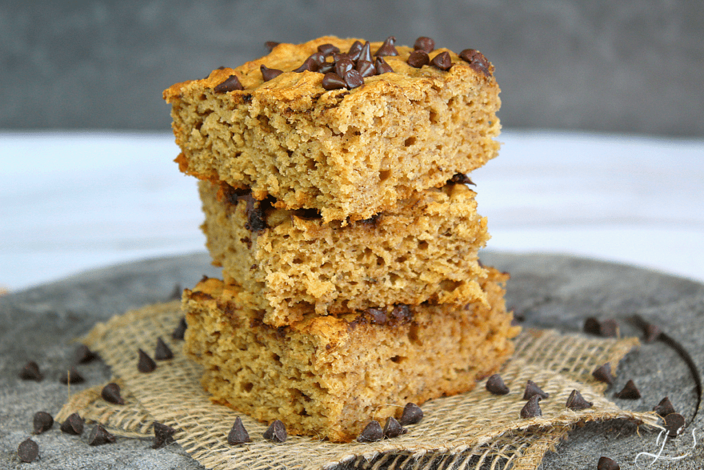 Chocolate chip blondies made with bananas and Greek yogurt stacked three high and mini chocolate chips scattered about. 