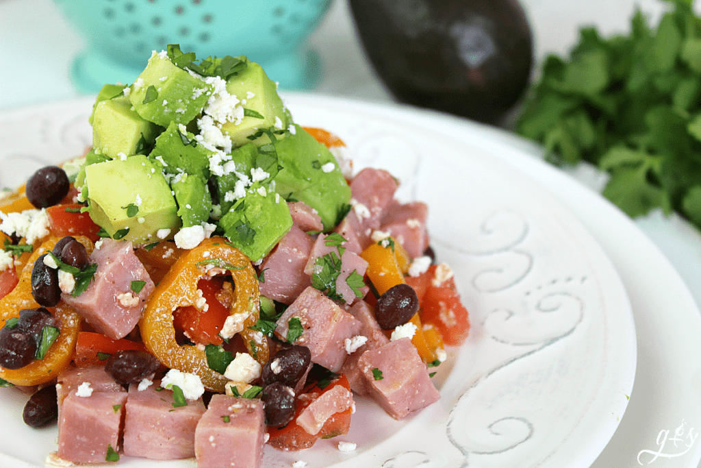 Chopped ham, black beans, mini bell peppers, and avocado salad stacked on a plate.