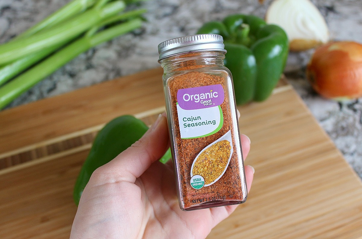 A woman's hand holding a bottle of Cajun seasoning.