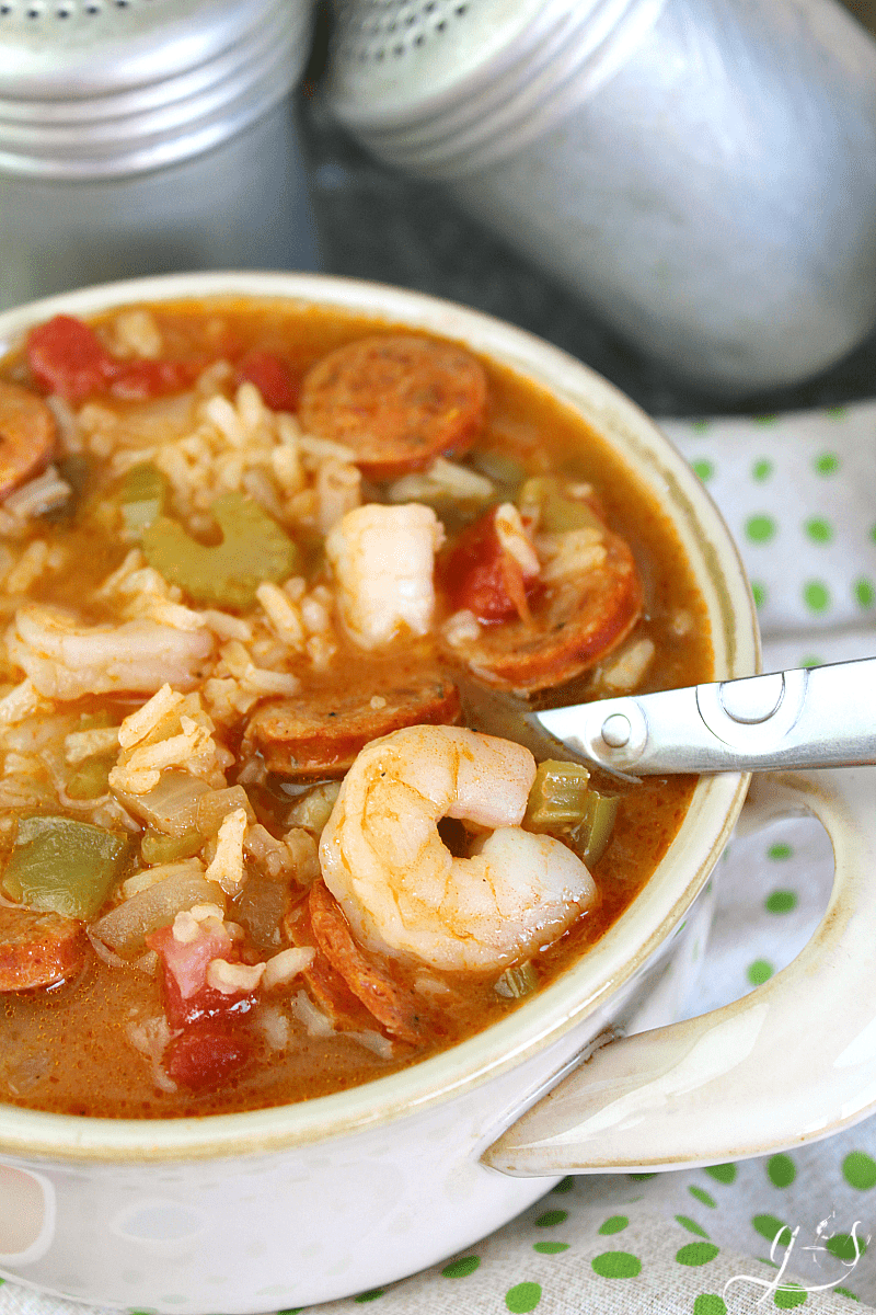 A spoon in a bowl of Cajun gumbo with shrimp and veggies.