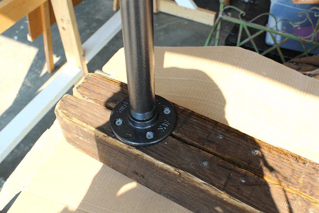 Securing flange and steel pipe to stained wooden banister for a rustic stair banister.