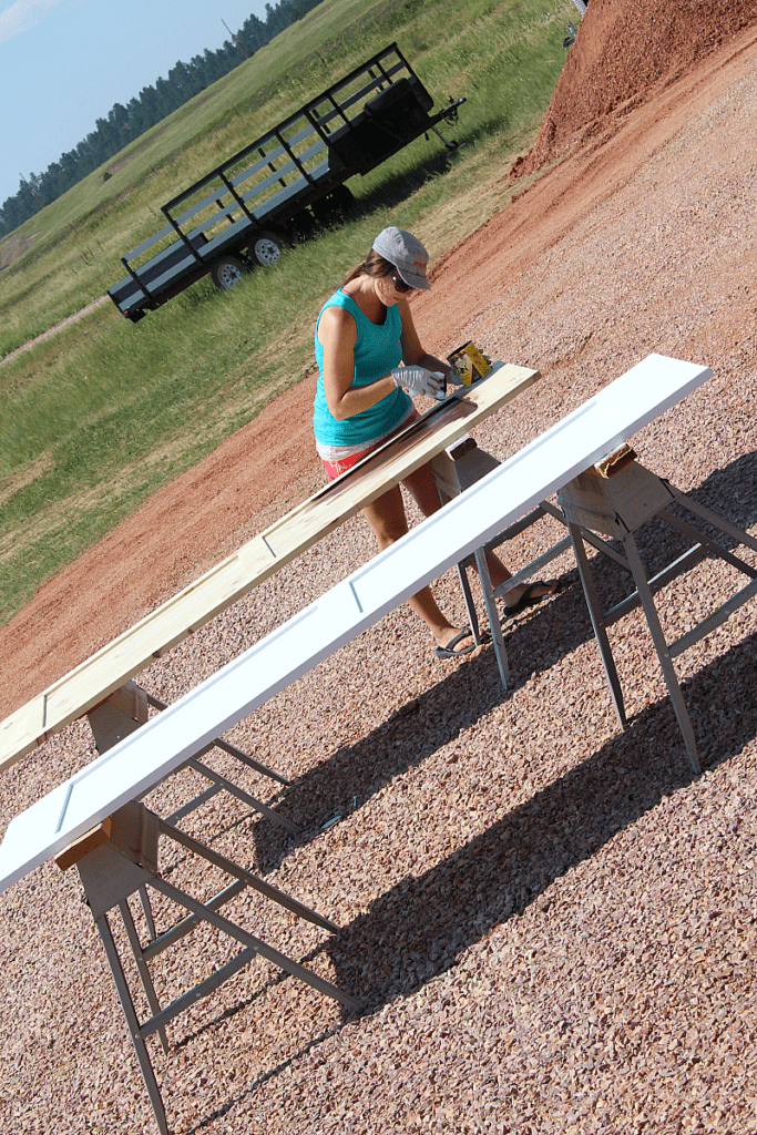 A white barn door and stained barn door with girl applying stain outdoors.