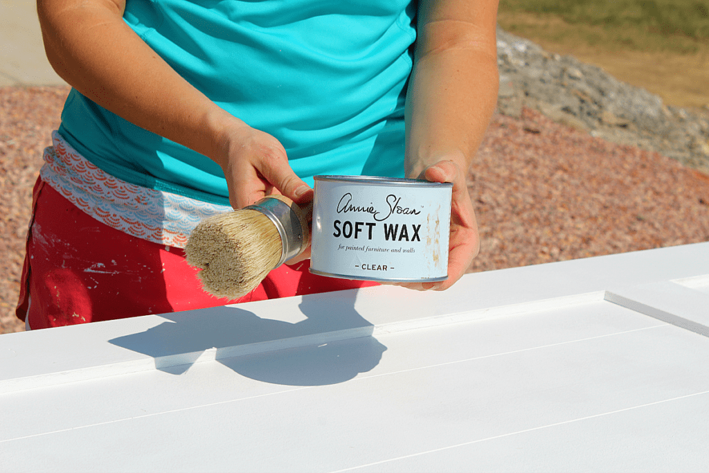 Annie Sloan Clear Soft Wax container with bristled brush to apply to white chalkboard barn door. 