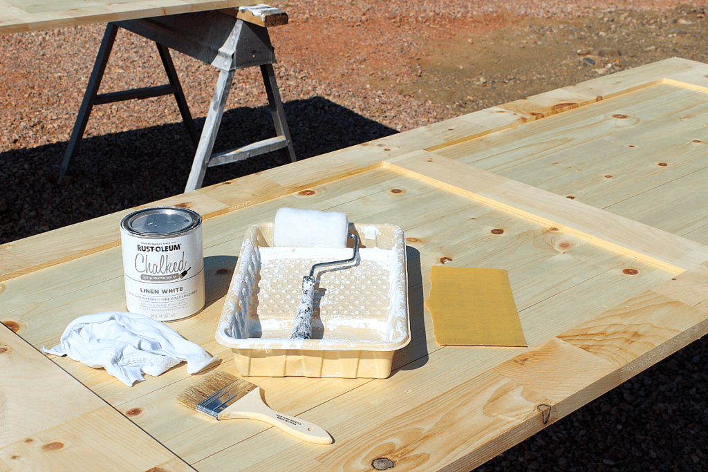 White chalk board paint, roller, brush, sand paper, rag atop barn door. 