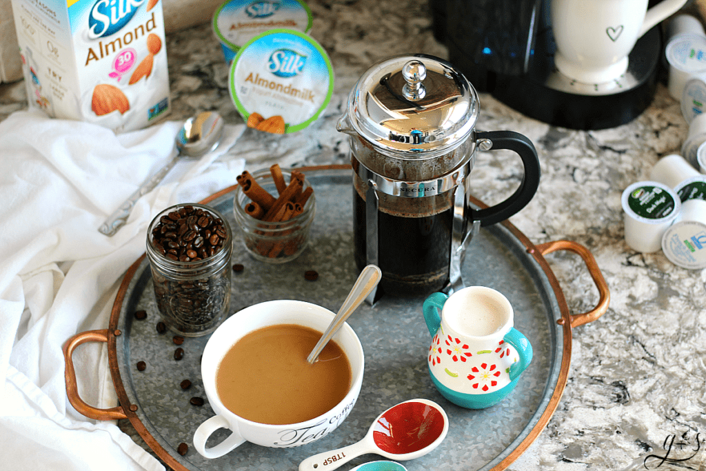A French Press coffee pot on a tray with a mug of coffee, cinnamon sticks, coffee beans, and Silk Almondmilk. The Keurig K-cups and Silk Almondmilk yogurt featured as well on a Bellingham Cambria Quartz counter top.