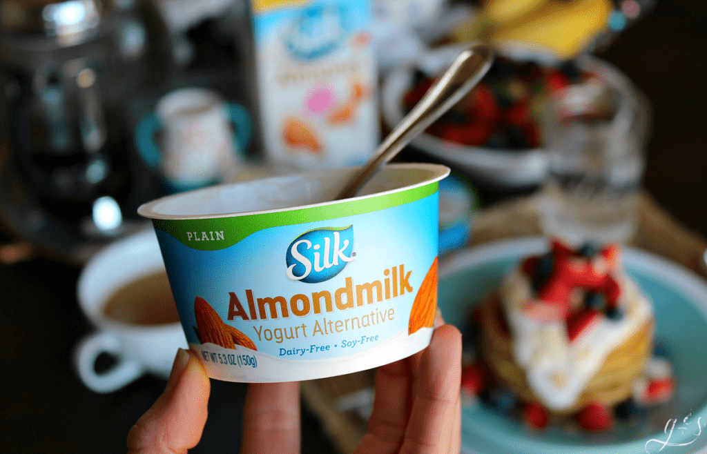 An up close image of plain Silk Almondmilk yogurt Alternative with Coconut Cake Pancakes in the background.