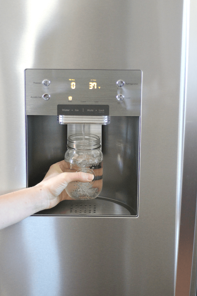 A stainless steel fridge dispensing water into a mason jar.