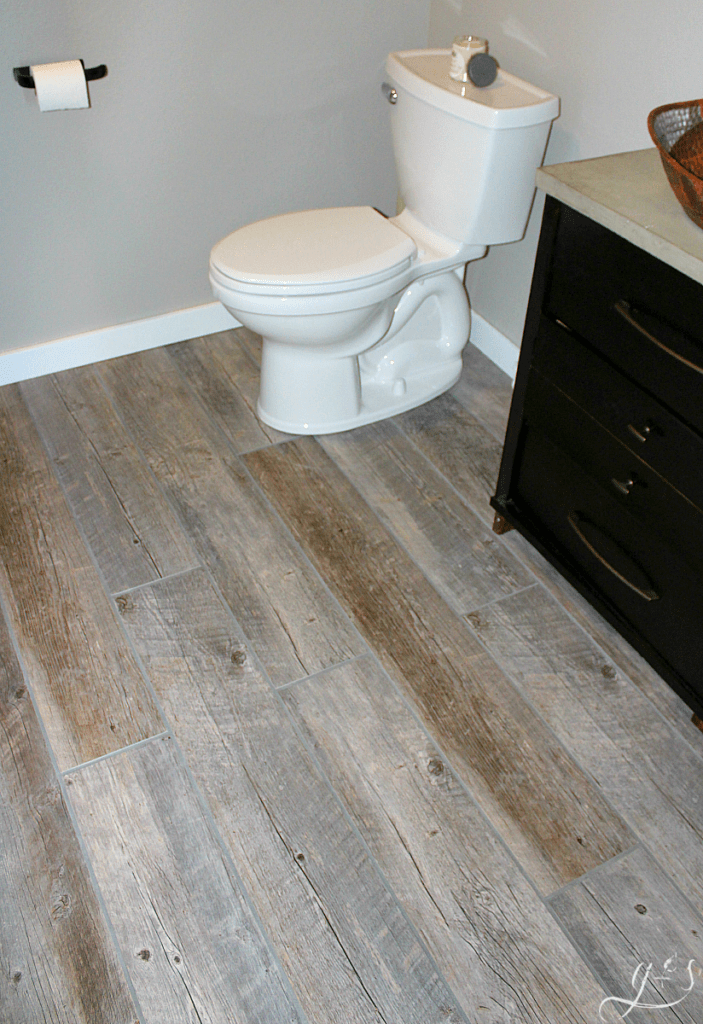 DIY How to Lay Floor Tile Planks | Our master suite bathroom floor is rustic and fun with the light tile that looks like wood and dark gray grout. These porcelain tile ideas and farmhouse designs are simple and beautiful. This tutorial to install your own large plank wood-look tiles on a budget will make you feel like a professional! I love the contrast of the grey-brown planks, white trim, dark vanity, and copper vessel sink. #farmhouse #tile #decor 