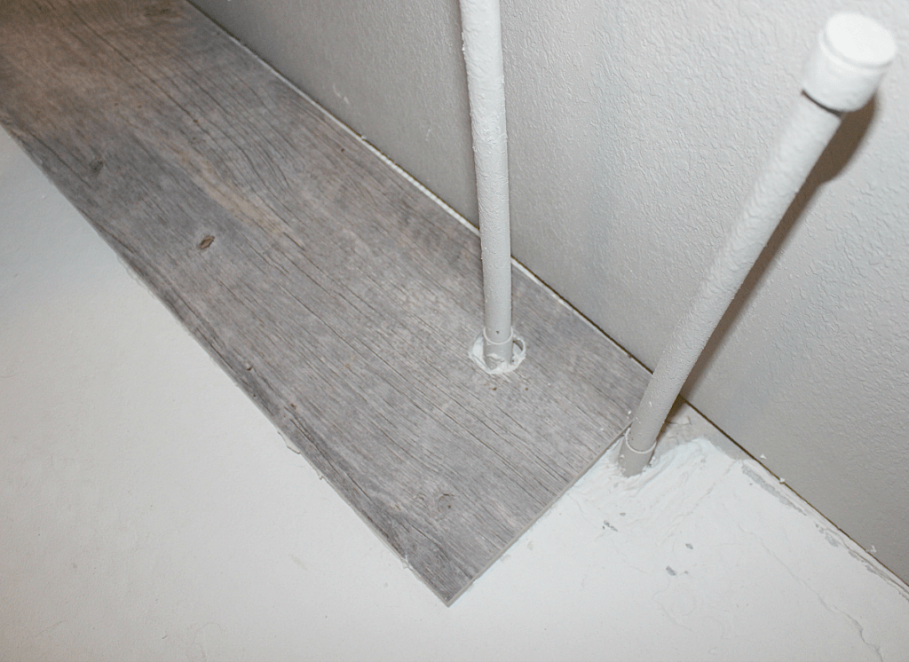 Long plank wood-looking tile with hole cut through it for water line. 