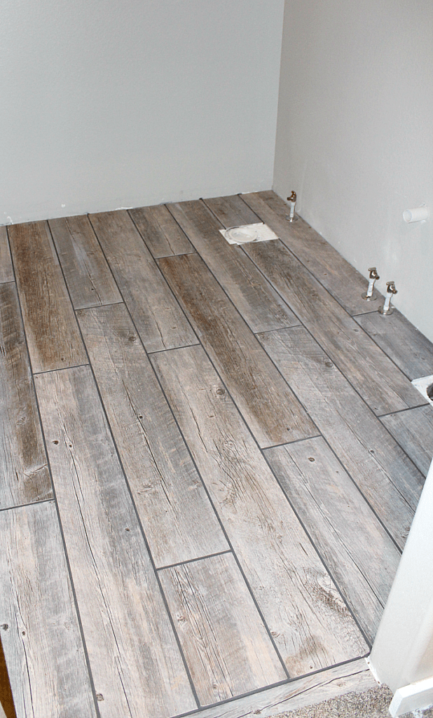 Wet grout lines in dark pearl grey between long porcelain tile planks in bathroom.