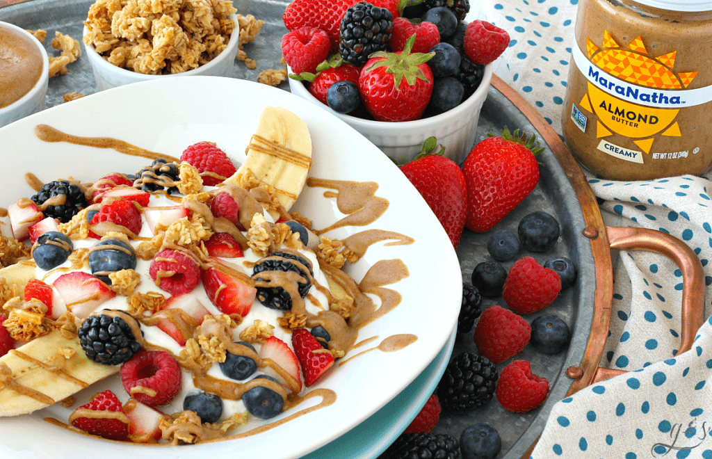 A Breakfast Banana Split plated on a metal tray with fruit, granola, and MaraNatha Almond Butter. 