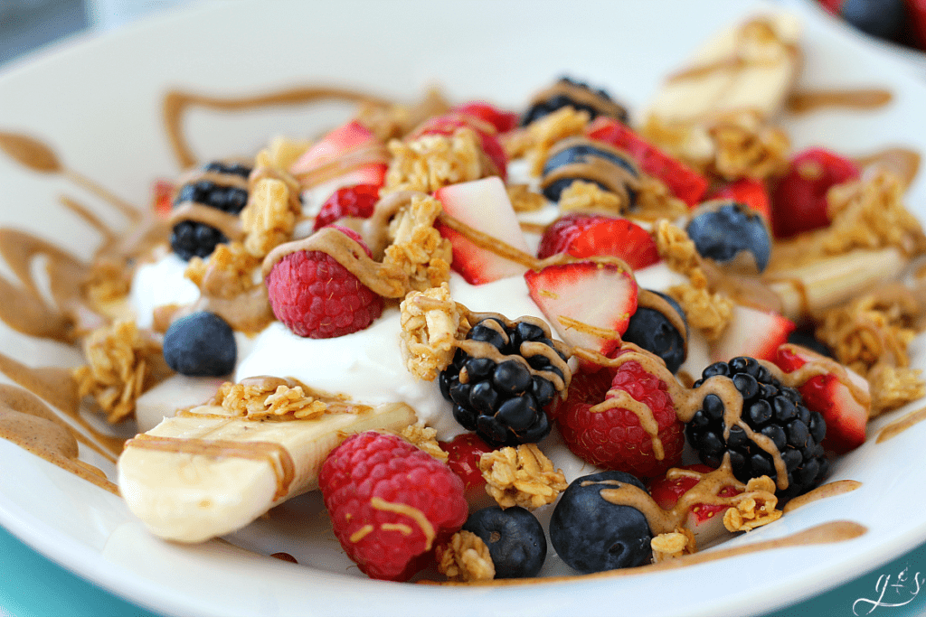 A close up shot of a breakfast banana split complete with a banana, berries, gluten-free granola, MaraNatha Almond Butter, and plain Greek yogurt. 