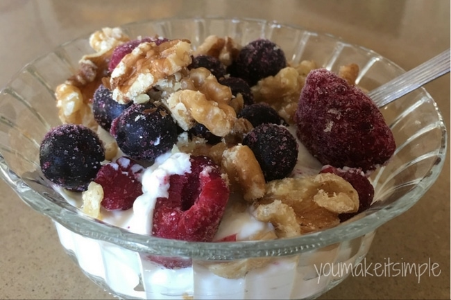 Plain Greek yogurt in a small bowl topped with frozen berries and pecans by You Make It Simple. 